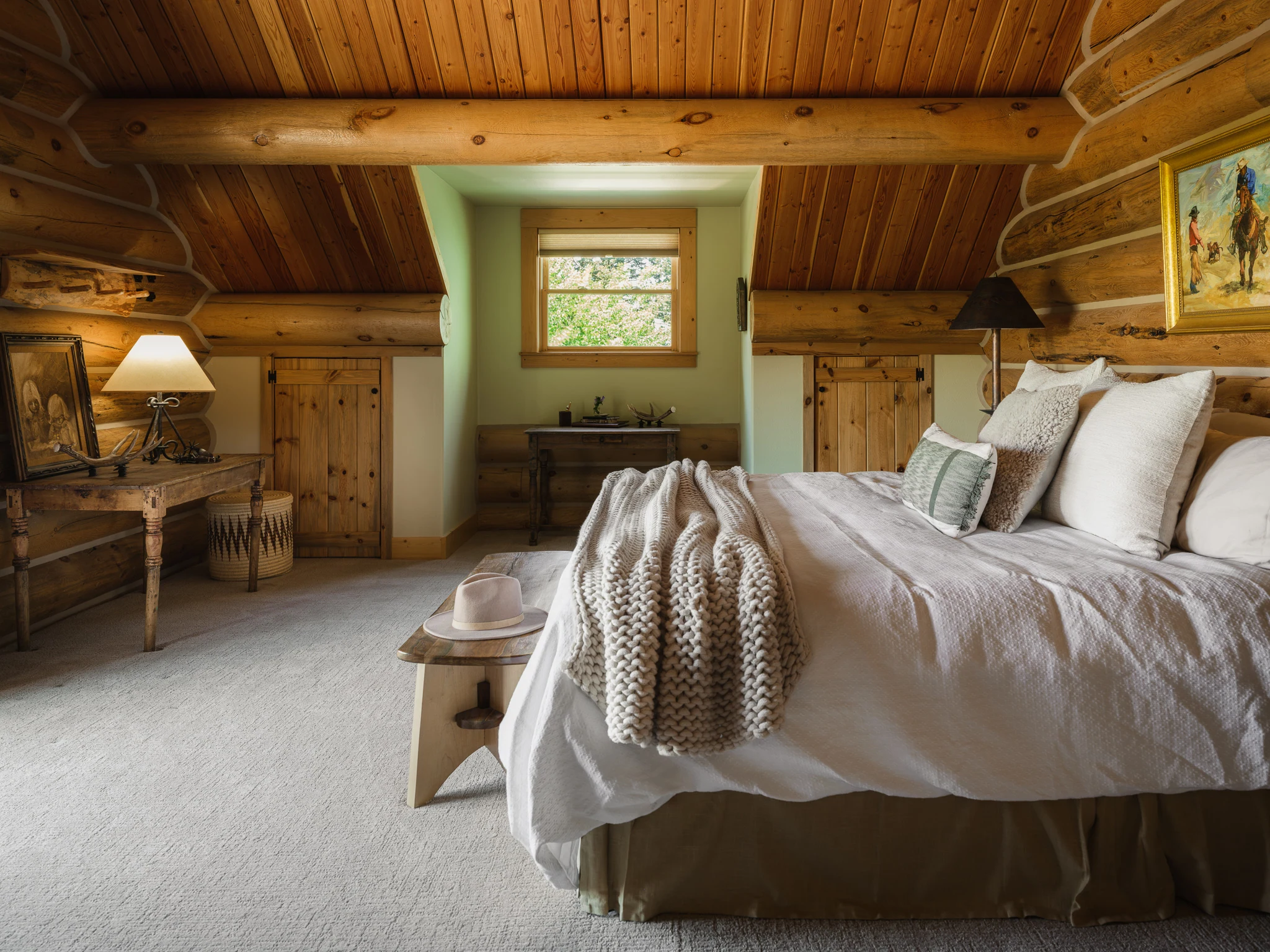 Bedroom beneath a vaulted log ceiling with an antique writing desk — interior design photography Livingston Montana, Sam Schlauch Designs